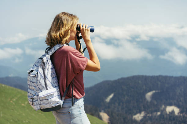 istock girl with a backpack in the mountains looking through binoculars 1264136212