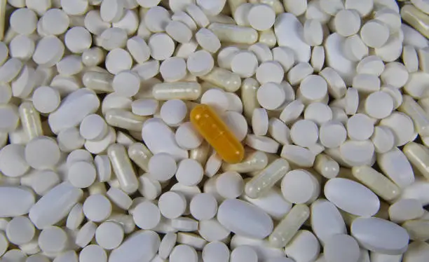 Full frame closeup of pile countless white pills and capsules with one yellow capsule in center (focus on yellow pill)