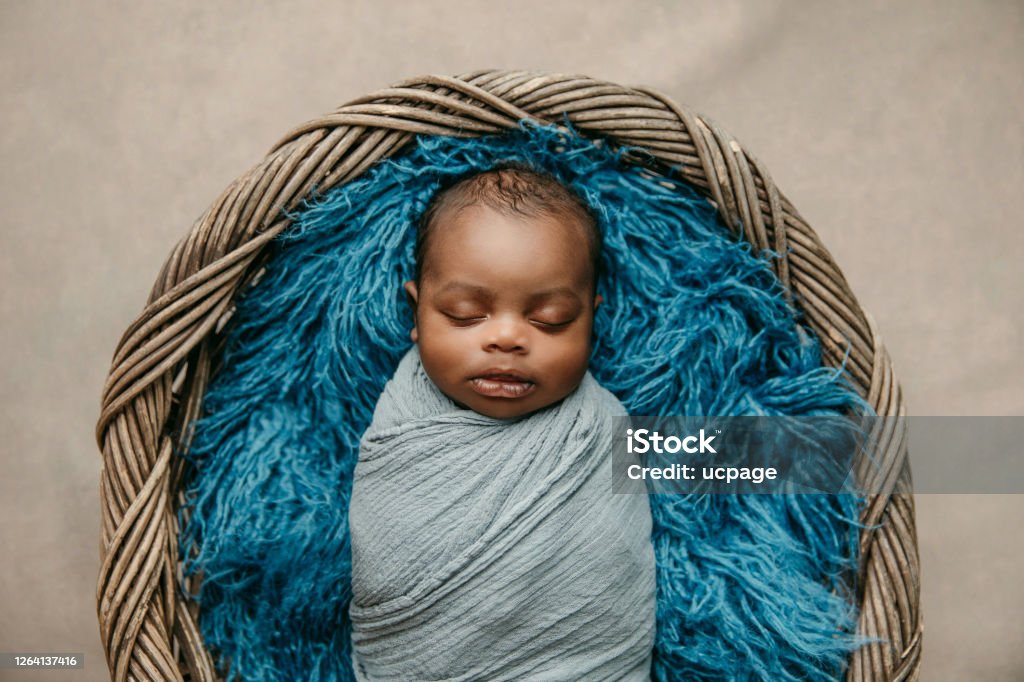 Sweet sleeping African-American newborn baby boy swaddled in a blanket and lying in a basket Baby - Human Age Stock Photo