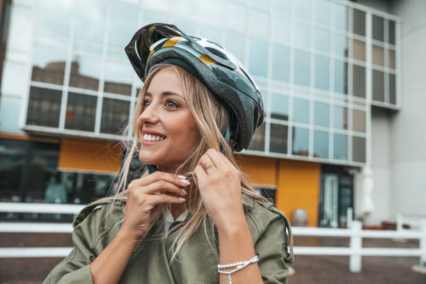 Woman putting helmet on and ready to ride Woman riding an electric scooter to commute to works place. Green incentive promoting the usage of electric scooters. cycling helmet stock pictures, royalty-free photos & images