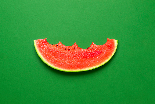 Single slice of watermelon top view on a green table. Eaten watermelon isolated on a colored background. Very juicy and refreshing summer fruit.