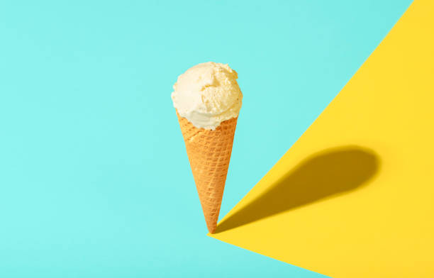 Vanilla ice cream cone in bright light. Waffle cone ice cream on summer colors Ice cream in a waffle cone with vanilla, on blue and yellow pastel background, in harsh light. Cold summer dessert. Just one vanilla ice cream cone. low carb diet photos stock pictures, royalty-free photos & images
