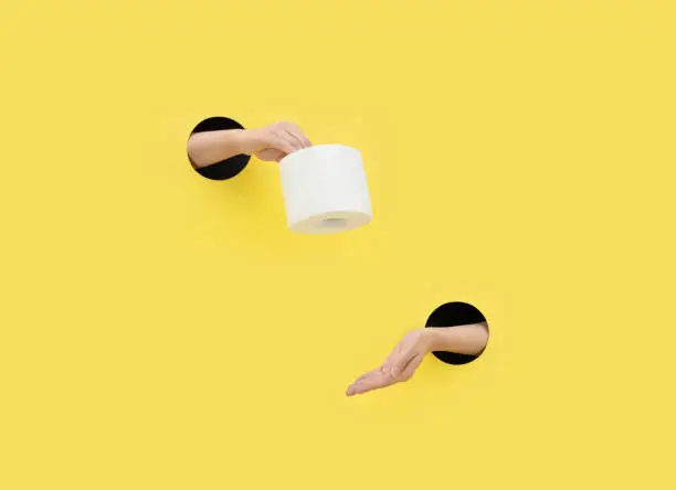 Photo of A female hand gives toilet paper on a yellow background. Hand in a paper hole. Help concept.