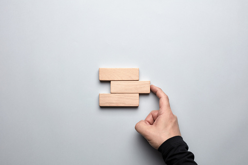 Male hand completing the gap between the wooden blocks. Concept of to accomplish a goal or to find a solution in business.