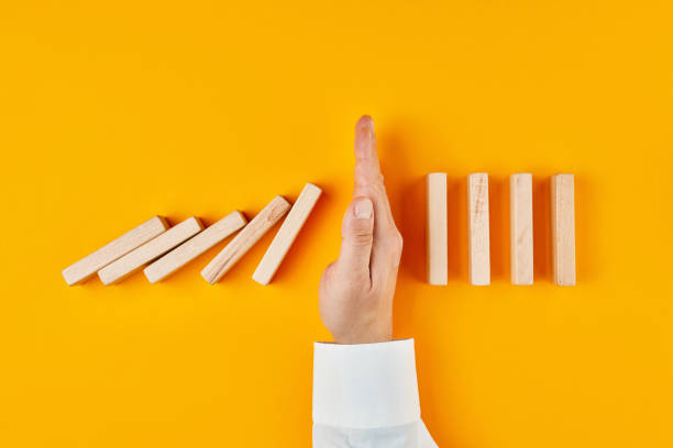 Hand of a businessman stopping domino effect on yellow background Hand of a businessman stopping domino effect on yellow background. Concept of risk protection, business solution or successful intervention strategy. domino stock pictures, royalty-free photos & images