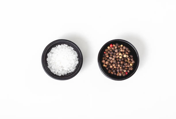 Salt and pepper in black bowl on white background. Top view