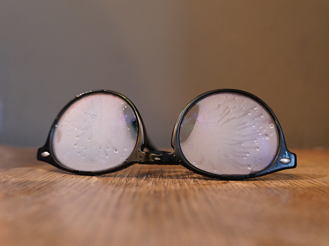 A set of eyeglasses lay on a wood table. The lenses are fogged up with moisture.