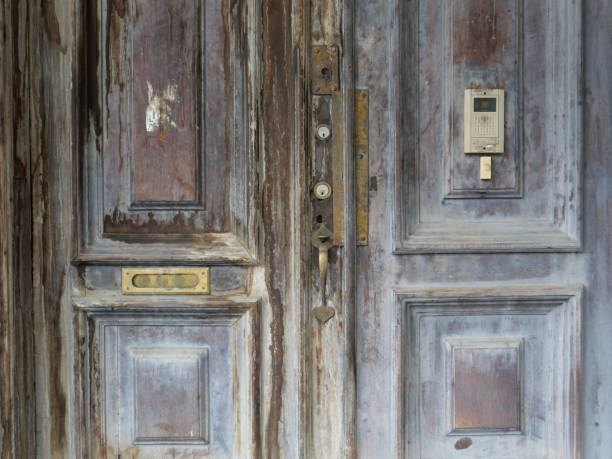 A rusty metal door handle is attached to a wooden door. The handle is secured to the door with a bolt. The handle is old and worn, with a few scratches and dents