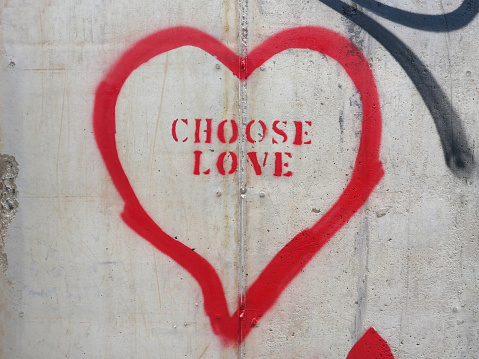 Painted sign on a cement wall has the message of Choose Love written inside of a heart.