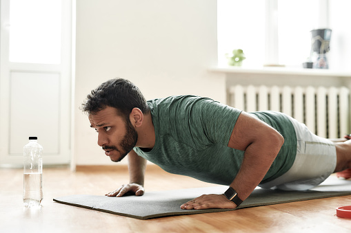 Fight for fit body. Young active man looking focused, exercising, doing push ups during morning workout at home. Sport, healthy lifestyle. Horizontal shot