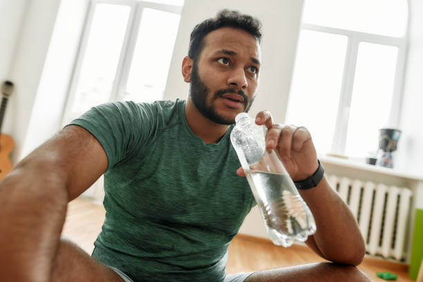 istock Hydrate. Young tired man looking away, holding water bottle in his hand while resting after training workout at home. Sport, healthy lifestyle 1264156896