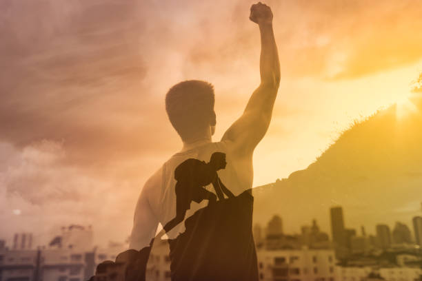 Strong young man in the city with fist in the sky climbing up a mountain. Reaching goals, and feeling motivated concept. Double exposure mental strength stock pictures, royalty-free photos & images