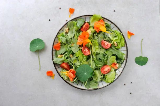 Salad with nasturtium leaves and flowers, salad leafs, tomatoes and nuts. Flat lay.horizontal. Background for different purpose.