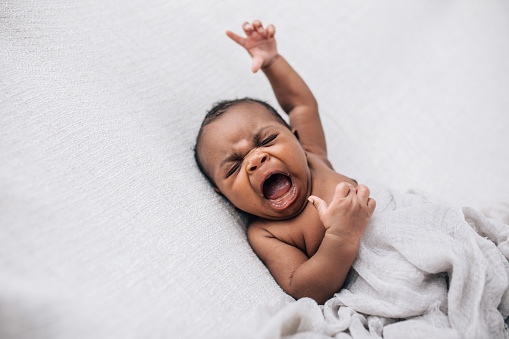 crying and upset and angry African-American newborn baby boy lying on a cream blanket