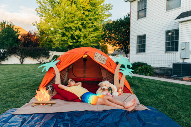 Beach Hut Backyard Staycation A dad with his son and young daughter camp out in the backyard of their home due to the coronavirus restrictions and quarantine. They have pitched a tent and created a beach scene with stuffed animal friends. They are making the best of their situation and long to return to the real outdoors. staycation stock pictures, royalty-free photos & images