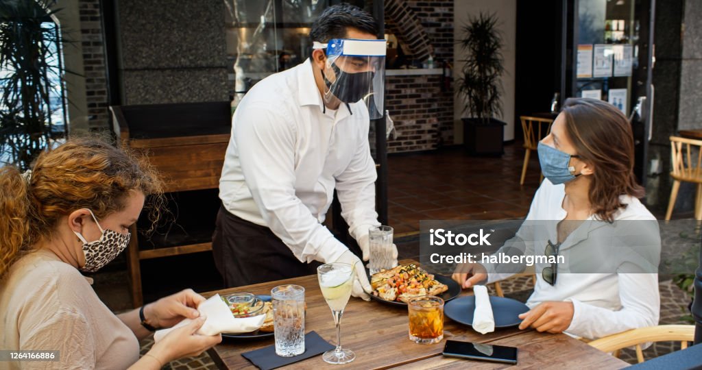 Waiter Wearing PPE During Covid-19 Pandemic Serving Food to Diners Wearing Masks A high end restaurant reopens after the 2010 Covid-19 lockdown, with measures in place to protect staff and customers. Restaurant Stock Photo