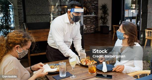 Waiter Wearing Ppe During Covid19 Pandemic Serving Food To Diners Wearing Masks Stock Photo - Download Image Now