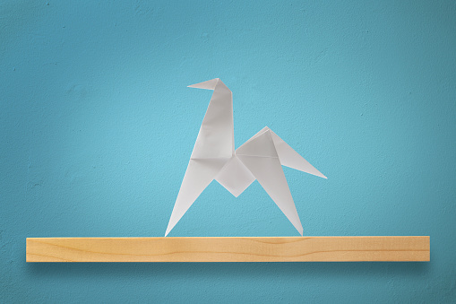 Blank origami horse on a wooden shelf against blue wall.