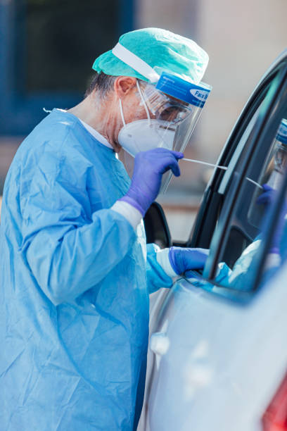 Medical personnel wearing a PPE, performing PCR with a swab in their hand, on a patient inside his car to detect if he is infected with COVID-19 stock photo