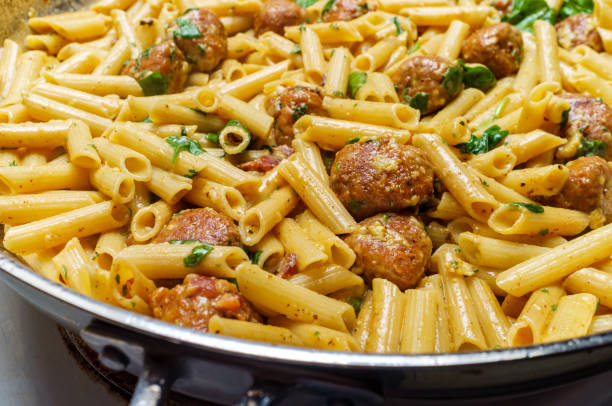 Italian Penne Carbonara Sausage Cooking Italian penne alla carbonara pasta in large pan on kitchen stove pecorino romano stock pictures, royalty-free photos & images