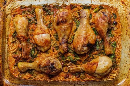 Cooking Spanish fideo con pollo chicken legs with vermicelli green olives and kale in large casserole dish
