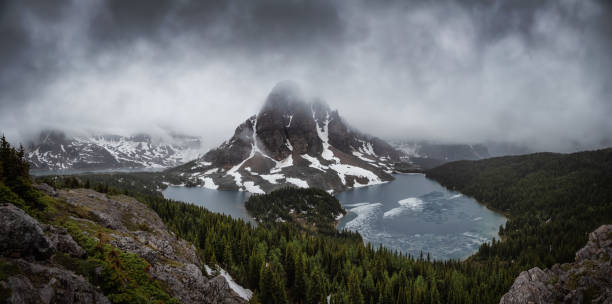 Beautiful panoramic View of the Iconic Canadian Rocky Mountain Landscape Beautiful panoramic View of the Iconic Canadian Rocky Mountain Landscape during a Dark and Moody Sunset. Taken near Banff, boarder of British Columbia and Alberta, Canada. Nature Background Panorama lake magog photos stock pictures, royalty-free photos & images