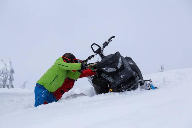 Squamish, British Columbia, Canada - January 18, 2020: Couple Adventurous people are recovering a flipped over snowmobile stuck in the snow.