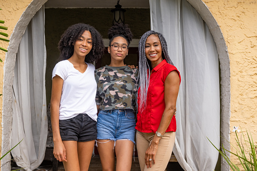 This is a portrait of a naturally beautiful African American mother in her 40s standing with her two Generation Z teenage daughters outside of their home in Miami, Florida.