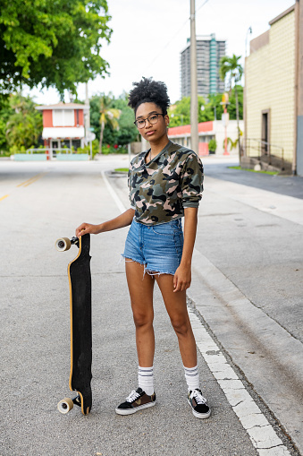 This is a photograph of a 14 year old teenage African American girl with natural hair skateboarding outdoors on a residential street in Miami, Florida.