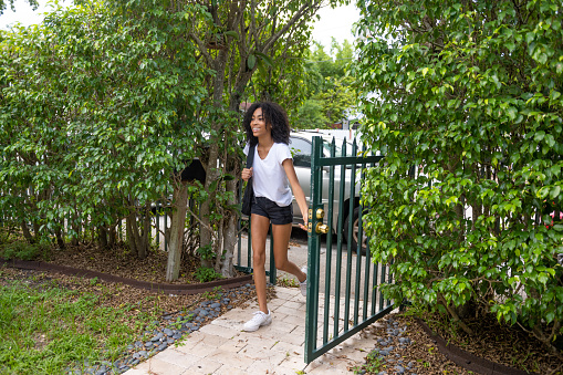 This is a photograph of a 17 year old African American teenage girl entering the front yard when arriving home with a backpack in Miami, Florida.