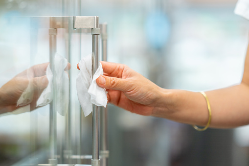 A close-up photo of woman`s hand while disinfecting the handle of a refrigerator in a supermarket before opening the door. She is disinfecting the handle of a refrigerator with a wet wipe alcohol.