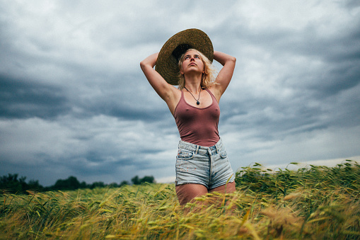 Photo of a young attractive woman standing in the middle of a wheat field while the storm is approaching