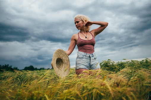 Photo of a young woman standing in the middle of a wheat field, walking away from her \