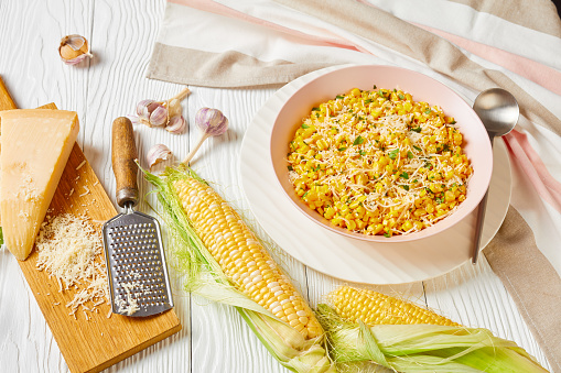 Rancho Parmesan Corn in a pink bowl on a white wooden table with ingredients, horizontal view from above,