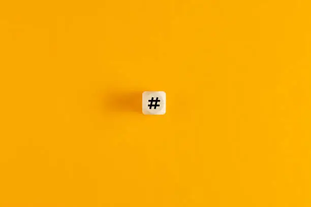 Photo of Hashtag symbol on wooden cube against yellow background. Overhead view with copy space.