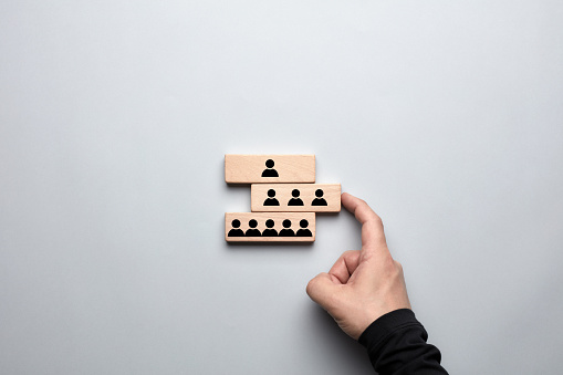 Organizational hierarchy or human resources strategy concept. Male hand pushing the wooden block with middle level employees and completing the corporate structure.