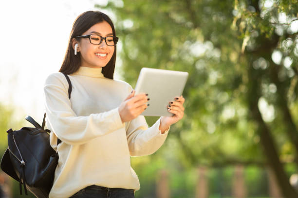 female student using tablet, standing in the park - filipino ethnicity audio imagens e fotografias de stock