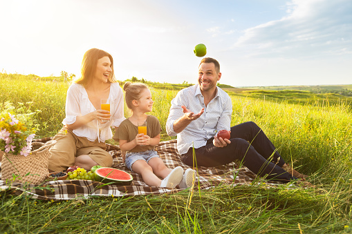 Portrait of excited guy juggling with apples, showing tricks to his family during picnic, free space