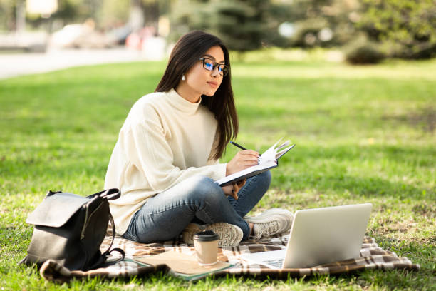 istock Girl writing in diary, using laptop, sitting in park 1264232082
