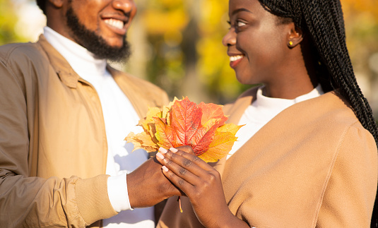 Romantic black couple with bunch of colourful leaves on date in autumn park, closeup
