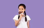 小さなアジアの女の子は、紫色の背景に立ってチョコレートを食べる、スタジオ