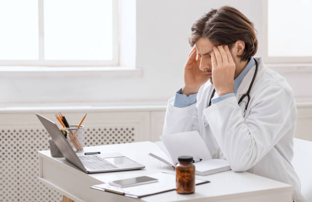 istock Overworked male doctor suffering from headache at workplace 1264235297