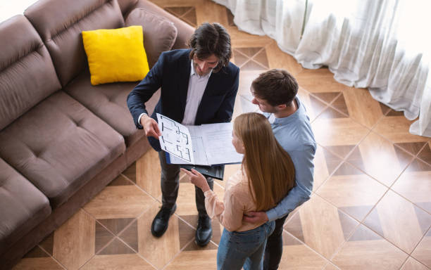 Real estate business. Above view of Real Estate Agent showing house plan to customers indoor Real estate business. Above view of Real Estate Agent showing house plan to customers indoors real estate agent male stock pictures, royalty-free photos & images