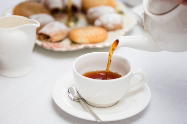 verser le thé anglais chaud dans la tasse de thé en céramique blanche - heure du thé photos et images de collection