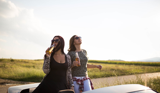Happy female friends toasting in a convertible at sunset