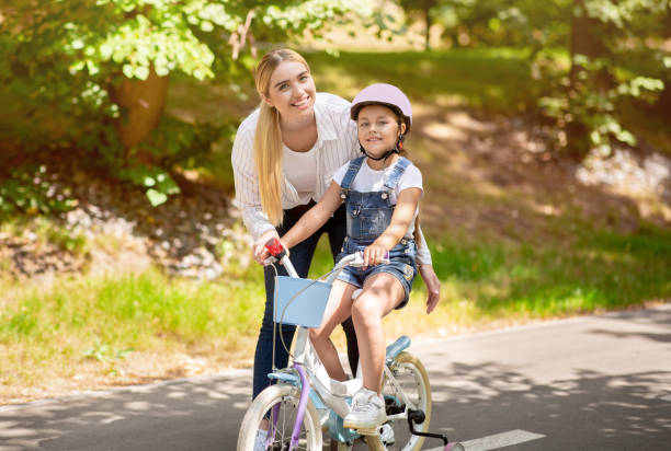 little daughter riding bike spending weekend with mother in park - helmet bicycle little girls child imagens e fotografias de stock