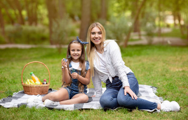 istock Mother And Daughter Blowing Soap Bubbles Sitting In Park 1264240525