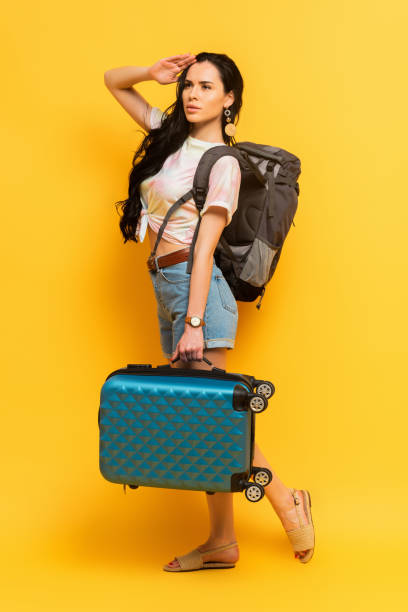 istock brunette woman with backpack and suitcase looking away on yellow background 1264240740