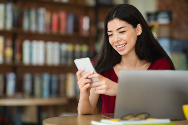 istock Smiling Asian Blogger Girl Using Smartphone In Cafe, Uploading New Content 1264240785