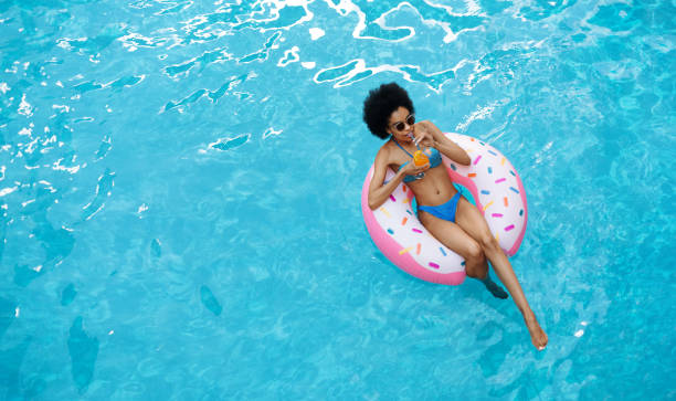 istock Relaxed black lady floating on inflatable ring and enjoying her cocktail drink at pool, top view. Space for text 1264242218
